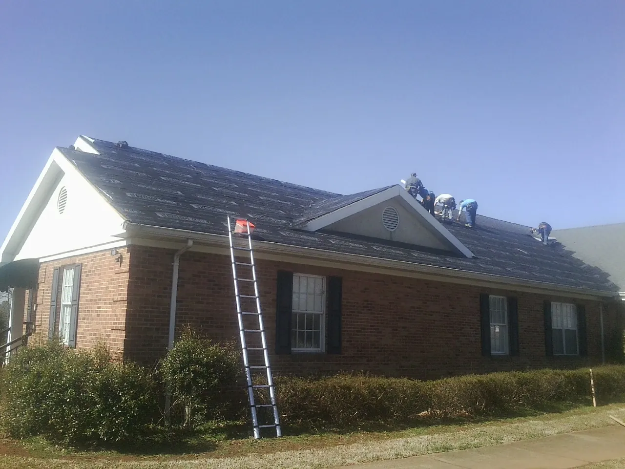 Crew tearing shingles off a brick ranch roof with a ladder set — Emergency Roof Repair work by our crew in Leesport
