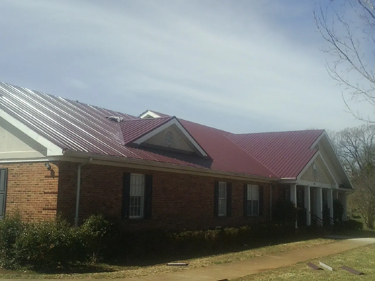 Red metal roof with gabled entries on a long brick building, from a Hail Damage Roof Repair job in Leesport