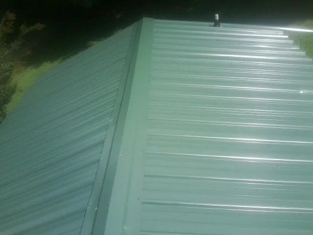 New green metal panels meeting at the ridge of a roof — Flat Roof Repair work by our crew in Leesport
