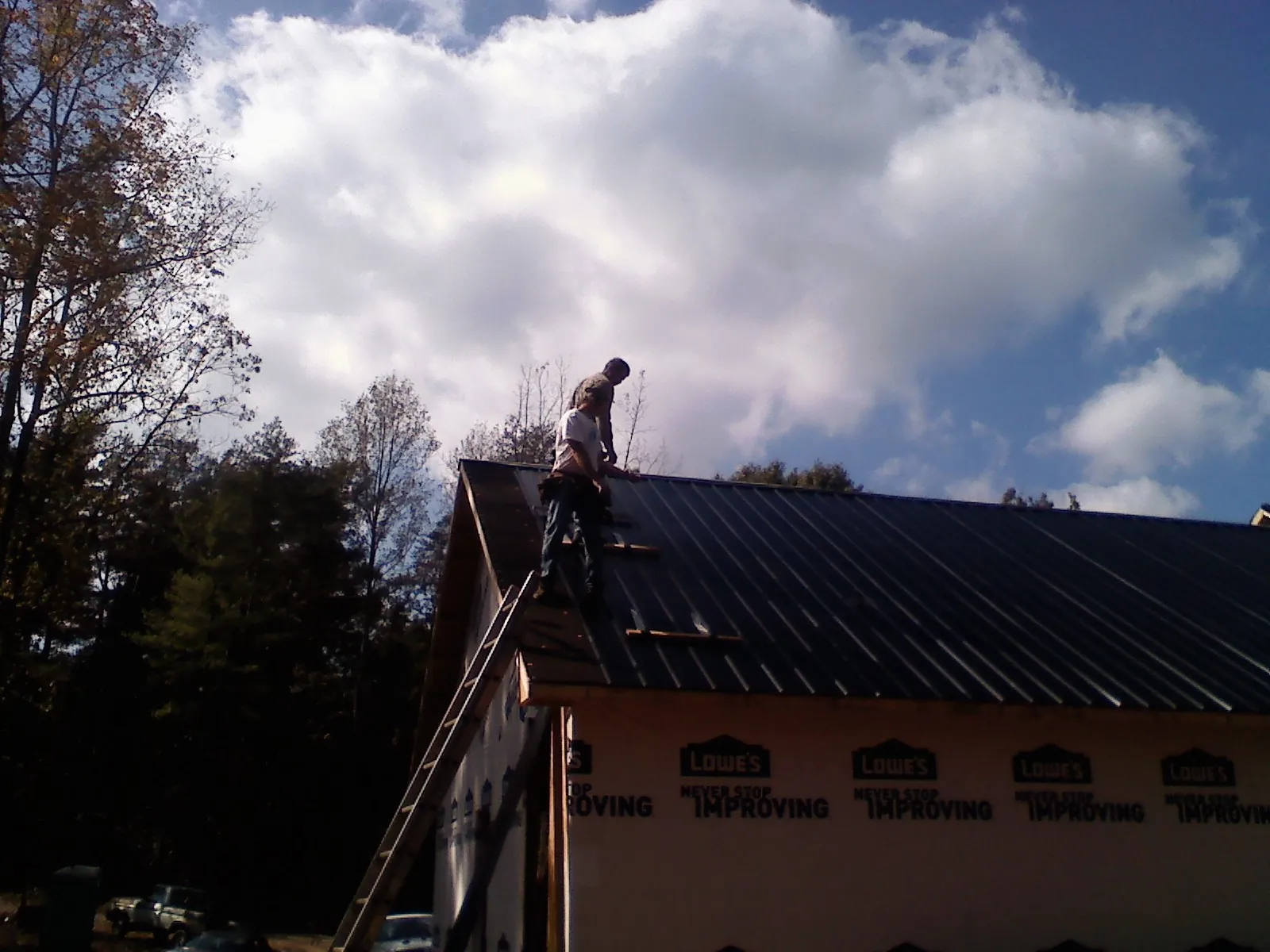 Roofer fastening dark metal panels high against a cloudy sky, from a Roof Inspection job in Leesport