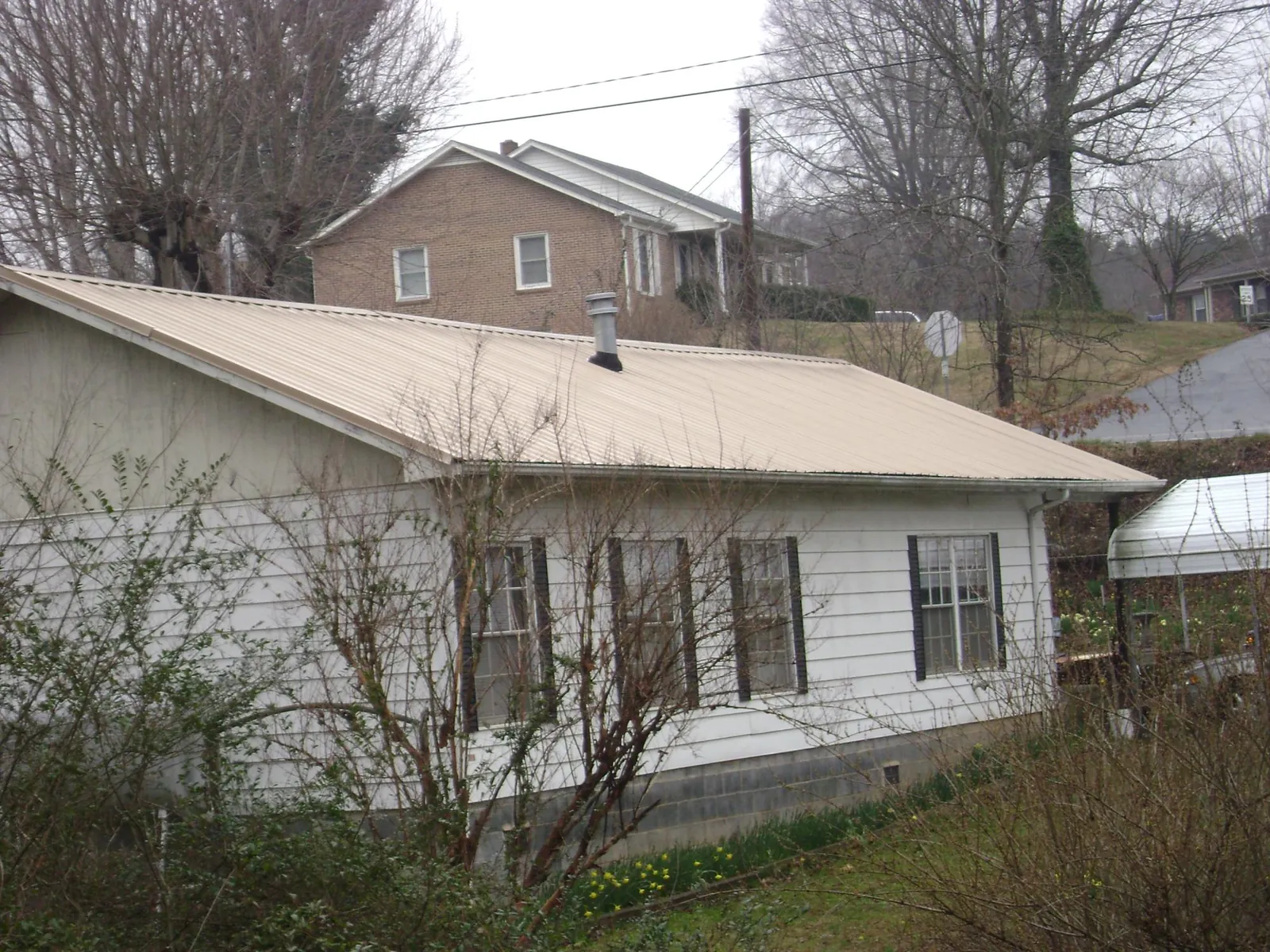 Tan metal roof on a white sided house set into a hillside — Commercial Roofing by Roofing Brothers in Leesport